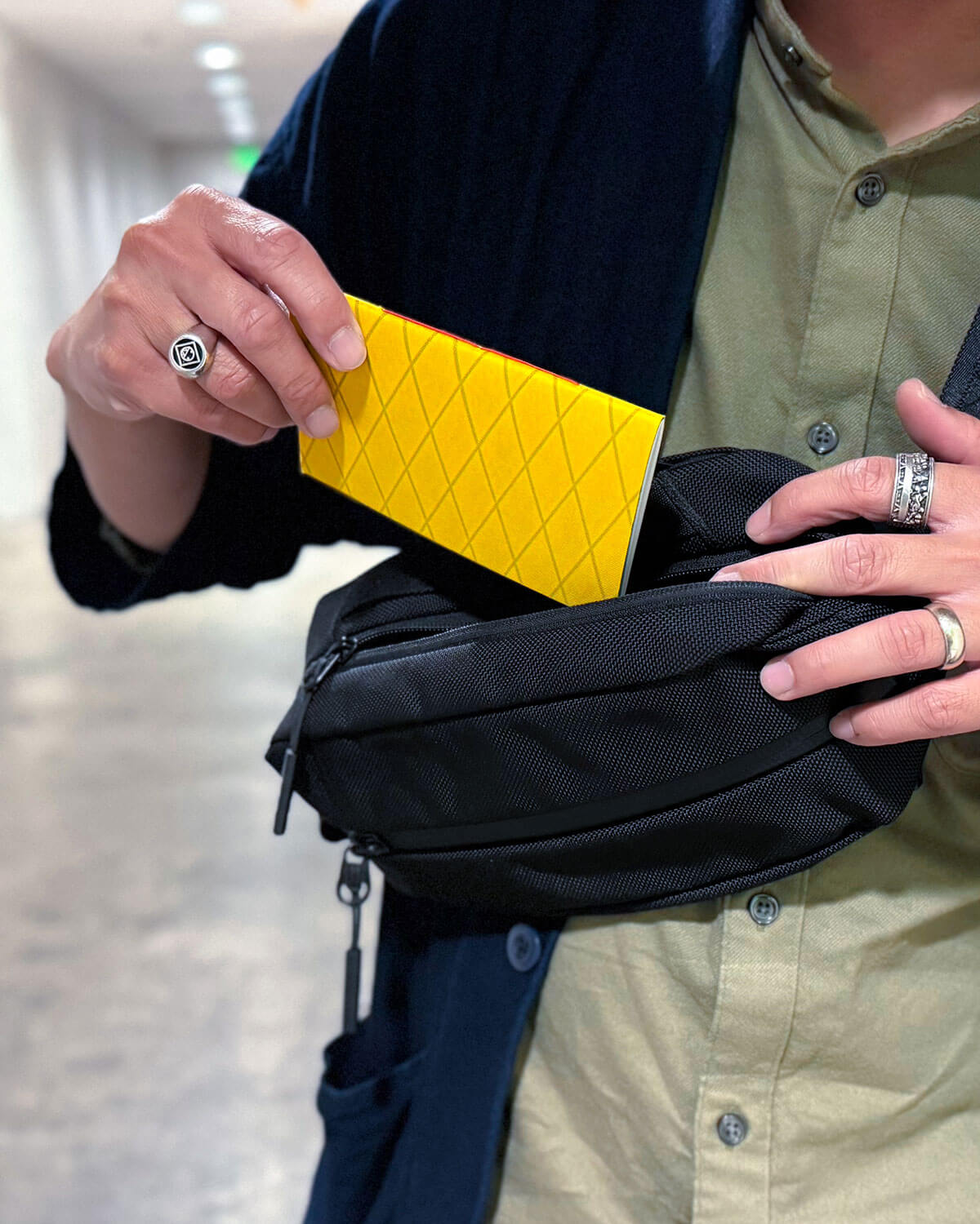 Person putting a Yellow Diamond Tactical Pockit Notebook into a black sling bag in a parking garage.